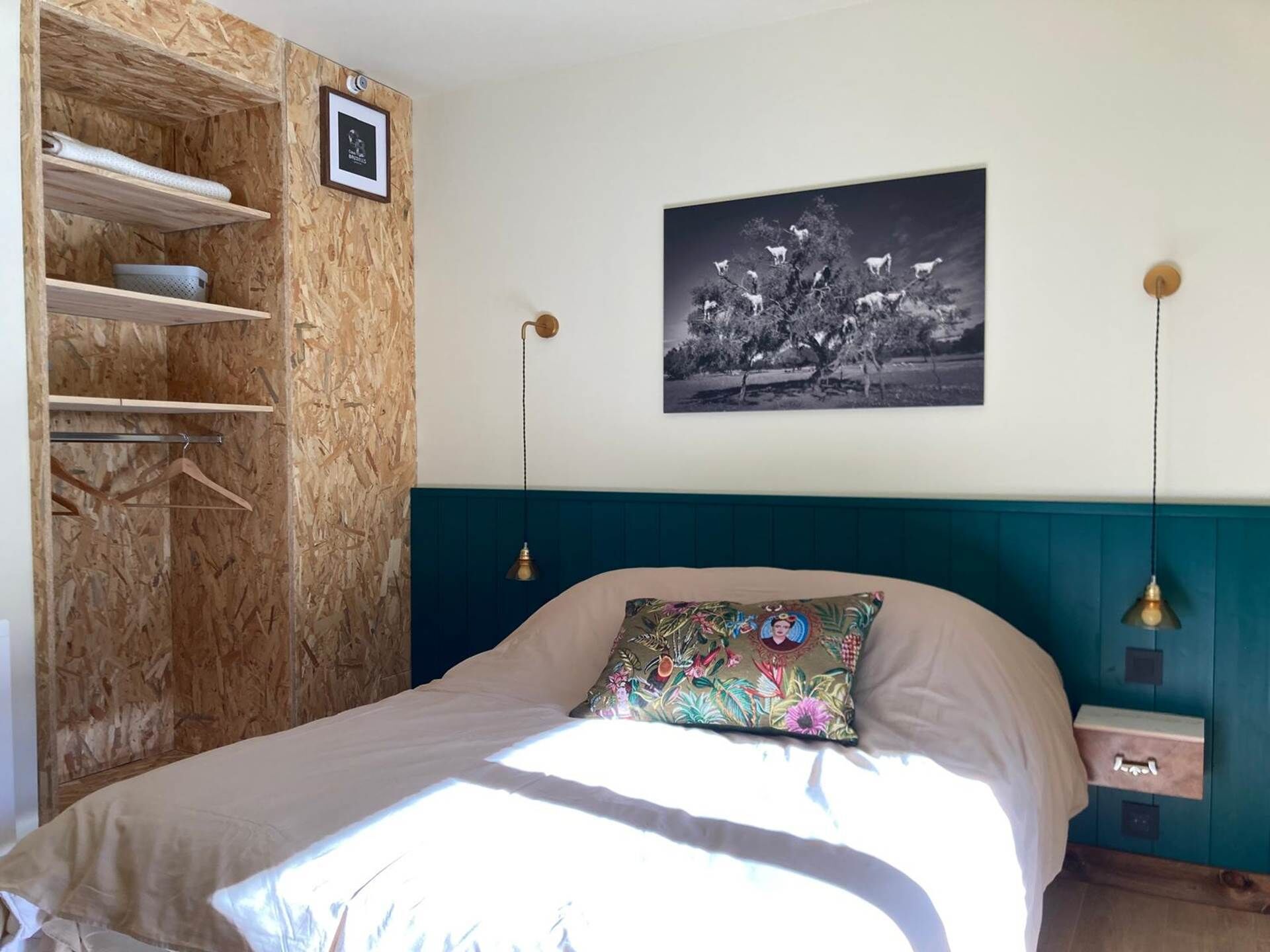 Ein Schlafzimmer mit einem Bett, einem Holzschrank, einem Wandbild und einem Nachttisch mit einer Lampe.