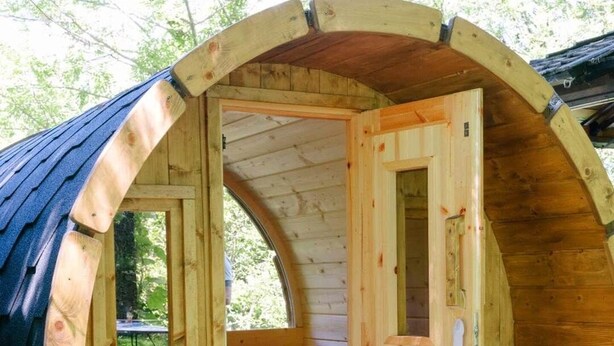 Una estructura en forma de barril de madera con una puerta, un banco y una ventana.