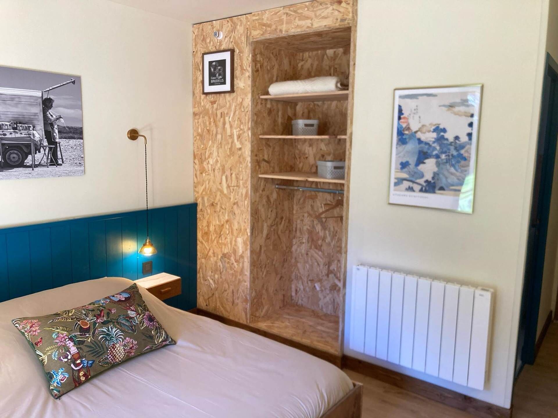 A bedroom with a bed, a wooden wardrobe, a radiator, and two framed pictures on the wall.