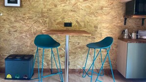 Een kleine kitchenette met een televisie aan de muur, twee smaragdgroene barstoelen en een tafeltje.