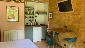 A compact room with a bed, a kitchenette, and a small dining area with stools.