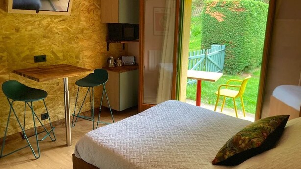 Een slaapkamer met een bed, een bureau, twee stoelen, een televisietoestel en uitzicht op een tuin door een schuifdeur.