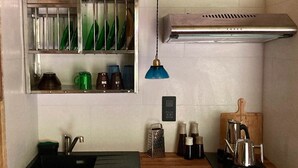 Ett litet, praktiskt kök med en diskho, en hylla med gröna och bruna muggar, en vattenkokare och en kaffebryggare.