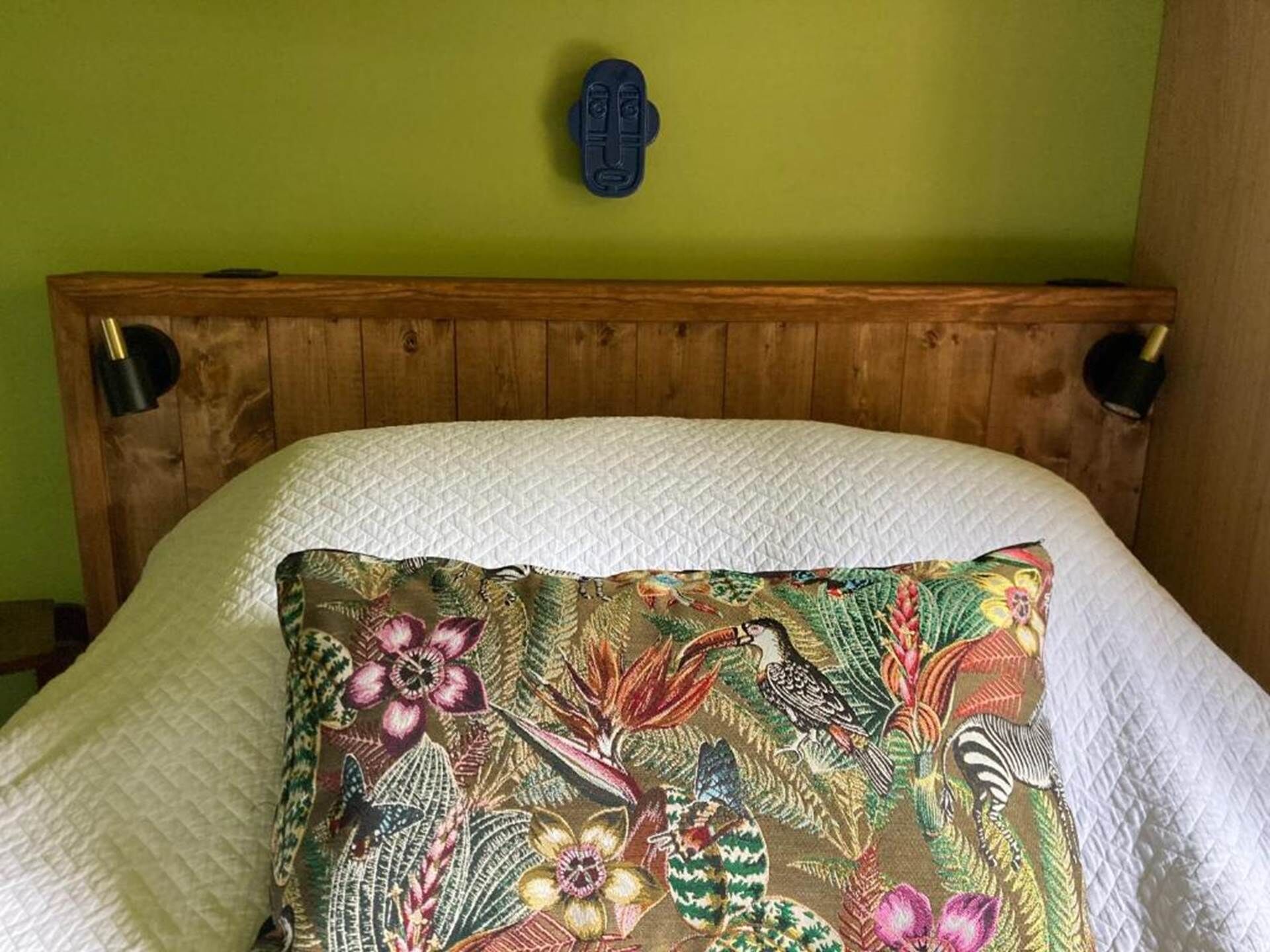 Un lit avec un oreiller à motifs floraux et une tête de lit en bois, le tout adossé à un mur vert.