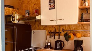 Eine kleine Küche mit Herd, Backofen und weißen Schränken. Auf der oberen Ablage stehen rote Töpfe und auf der Arbeitsplatte ein Kaffeeautomat.