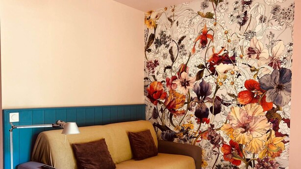 Ein Zimmer mit einem Bett, einer Nachttischlampe und blumigem Wandpapier.
