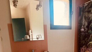 Ein Badezimmer mit einem weißen Waschbecken, Spiegel und Toilette. Über dem Waschbecken befindet sich ein Fenster und eine Duschvorhang mit einem Blumenmuster.