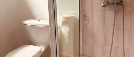 A bathroom with a toilet, a shower with a glass door, and a yellow trash bin.