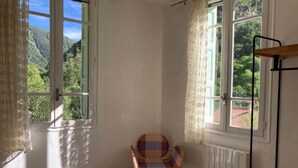 A bedroom with a bed, a chair, and two windows with curtains. - Studio (2 people) (SAHORRE)