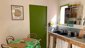 A small kitchen with a green door, a dining table with chairs, and a hanging pot rack above the sink. - Studio (3 people) (SAHORRE)