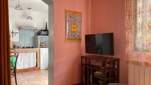 A living room with a television on a wooden stand, a kitchen in the background, and a poster on the wall. - Studio (3 people) (SAHORRE)