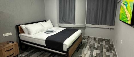 A bedroom with a bed, a nightstand, a ceiling light, and a window with curtains.