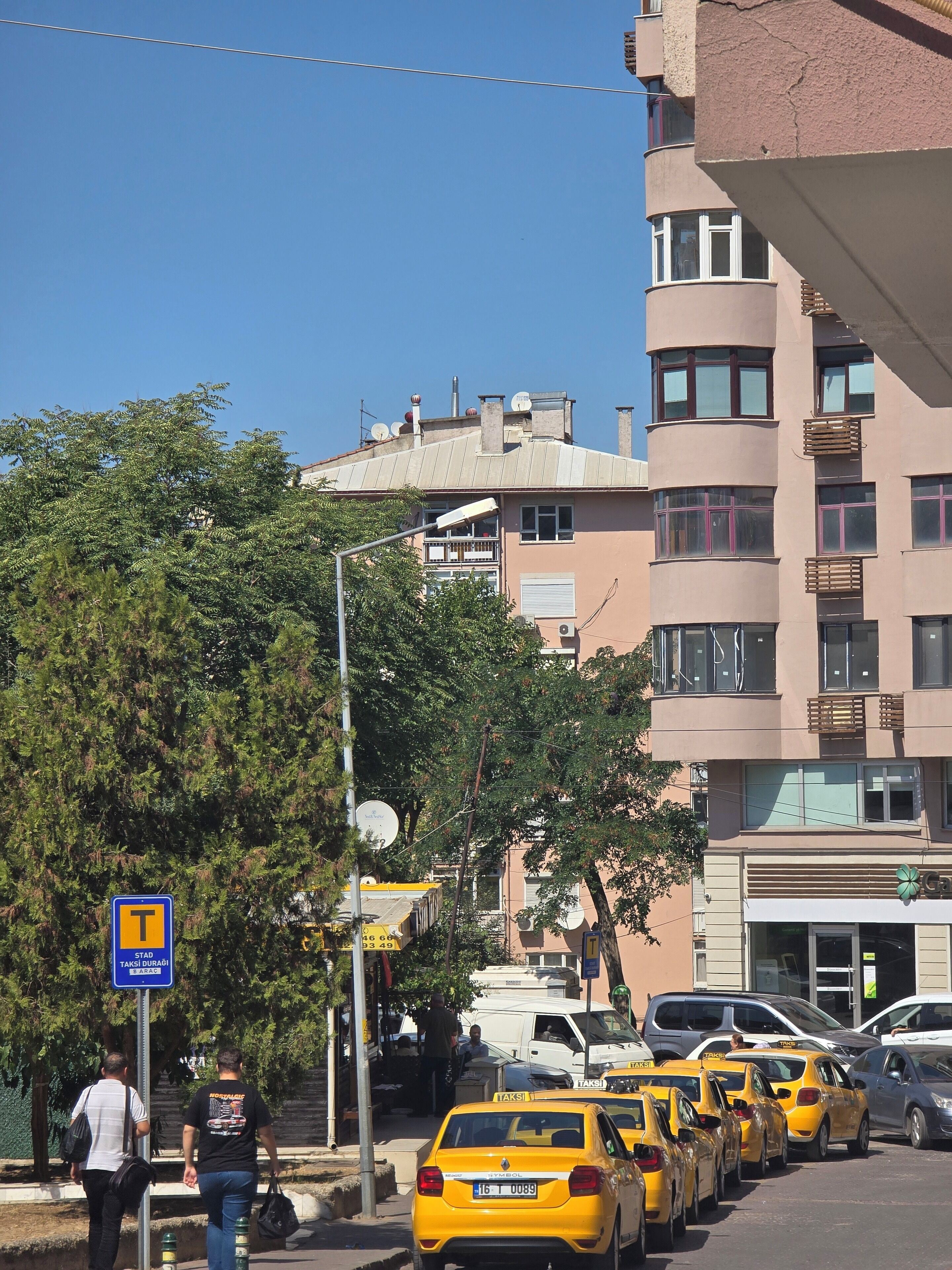 A row of yellow taxis parked on a city street with buildings in the background.