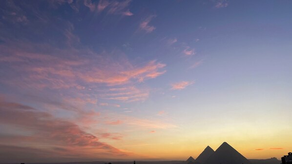 A desert landscape with pyramids silhouetted against a sunset sky. - asser hotel pyramids (Giza)