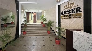 A hotel reception area with a staircase leading to the upper floors, potted plants, and a sign indicating the hotel's name and view. - asser hotel pyramids (Giza)
