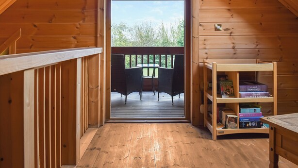 A wooden interior with a balcony, a table, and a bookshelf.