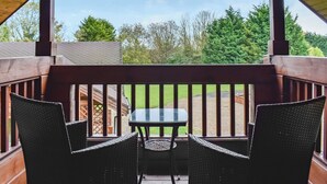 A covered outdoor seating area with two wicker chairs and a small table, overlooking a grassy yard and trees.