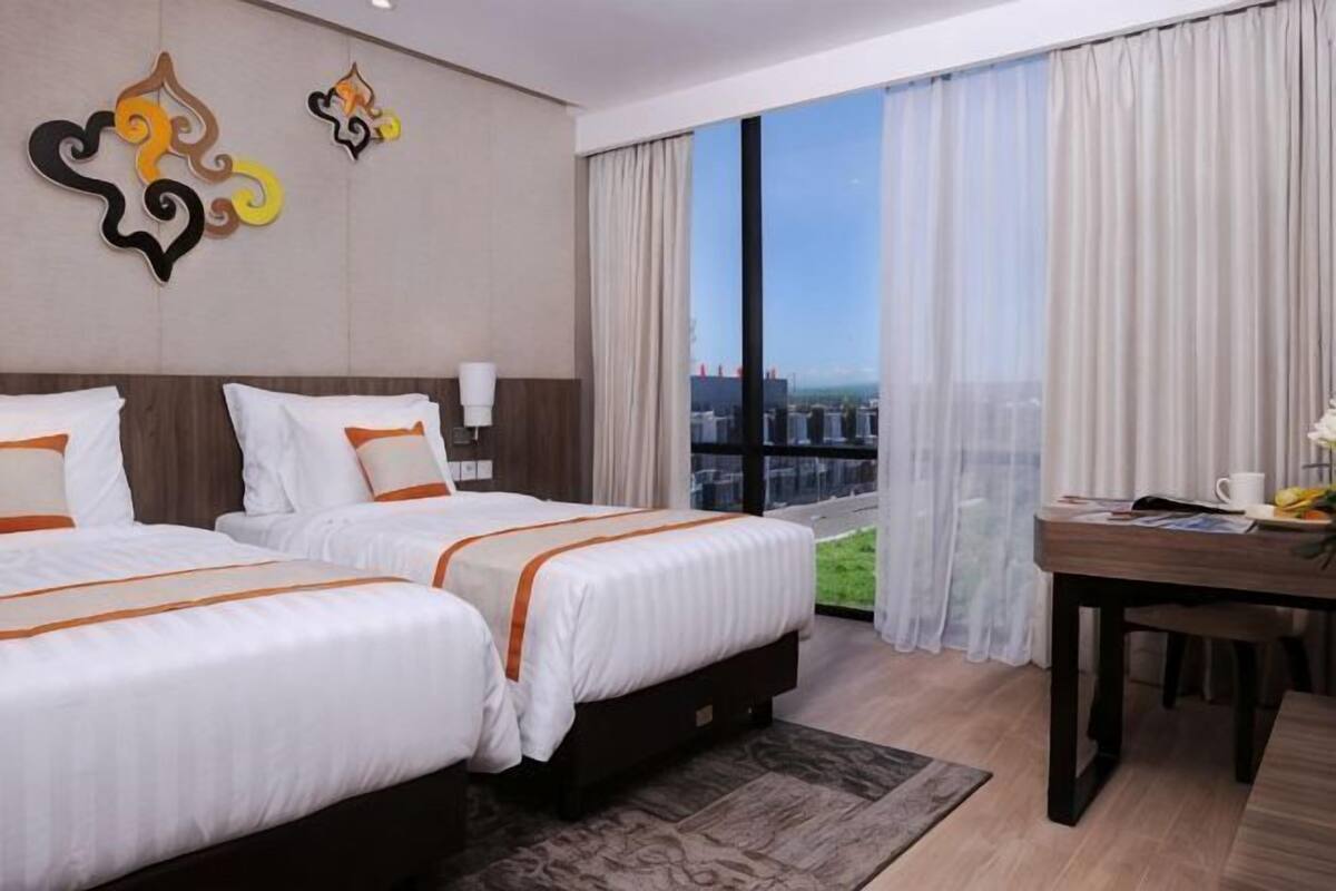 Quarto de hotel com duas camas, uma escrivaninha e uma janela grande com cortinas.