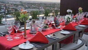 Een gedekte tafel voor een maaltijd, met wijnglazen, borden en rode servetten, met uitzicht op een stadsgezicht.