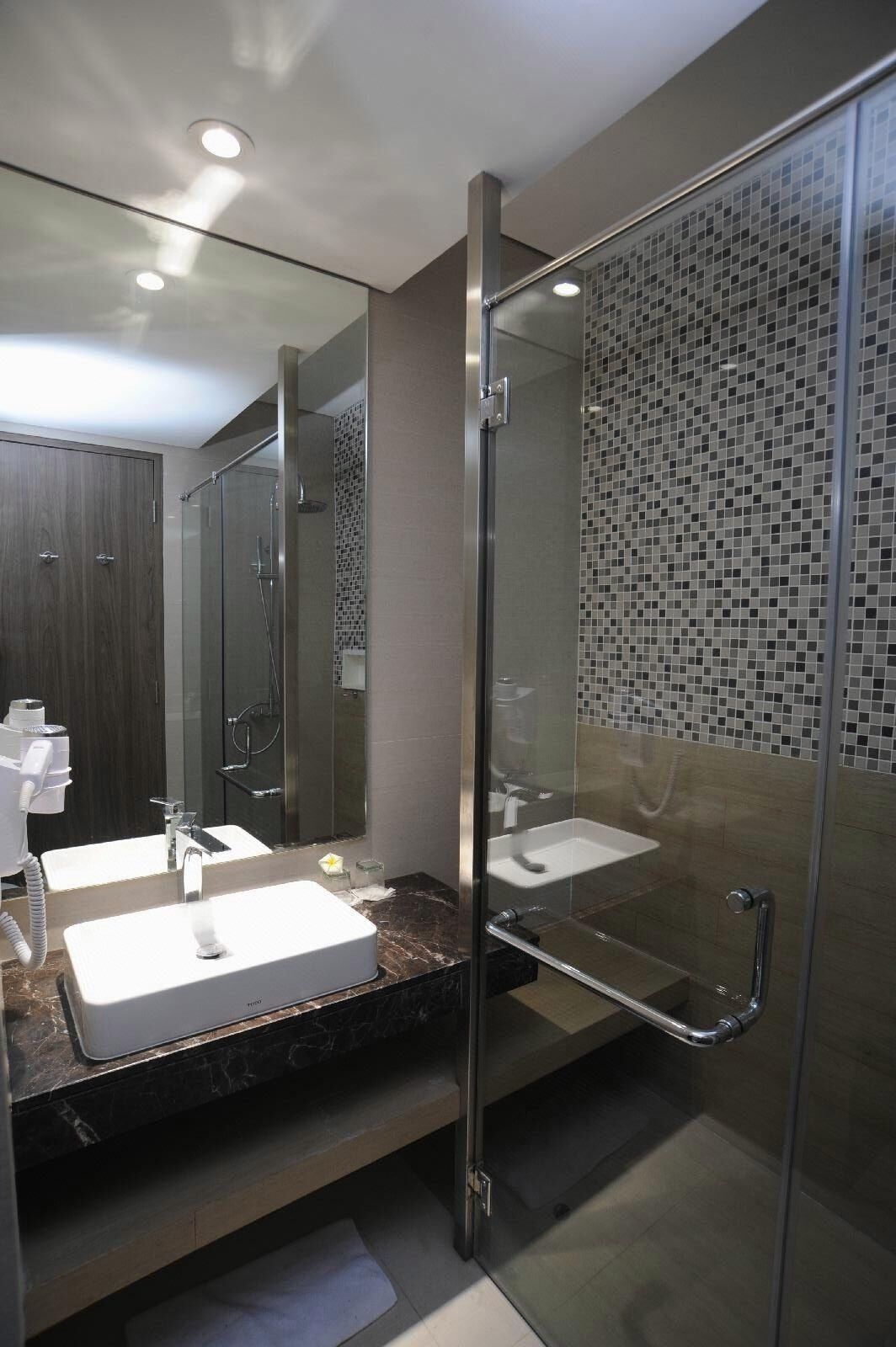 Un baño moderno con ducha envuelta en vidrio, un espejo grande y encimera de mármol.