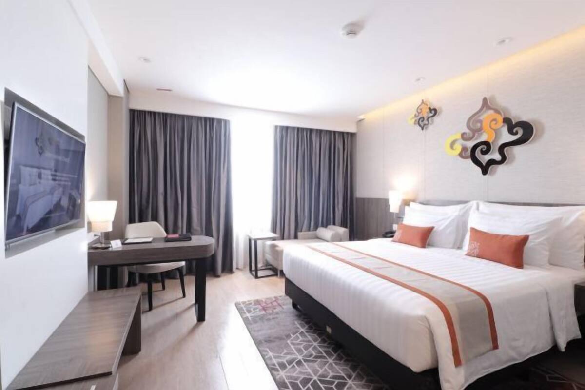 Quarto de hotel com cama, escrivaninha, cadeira, televisão e cortinas.