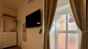 Een kamer met een wandgemonteerde flatscreen televisie, een houten dressoir en een deur naar een buitenruimte met een bakstenen muur.