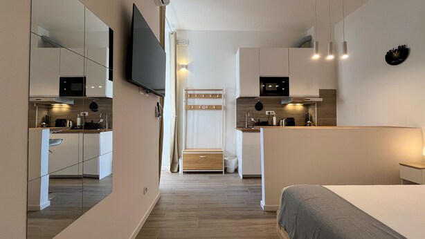 Een moderne, compacte hotelkamer met een kitchenette, een bed en een televisie.
