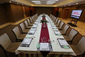 Una sala conferenze con un lungo tavolo apparecchiato per una riunione, circondato da sedie.