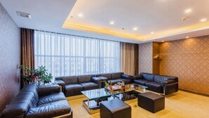 A modern living room with a sectional sofa, a glass coffee table, and a large window with curtains. - UPLS Hotel (Zhongwei)