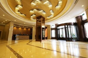 A spacious lobby with a polished floor, a reception desk, and a large, curved glass entrance. - UPLS Hotel (Zhongwei)