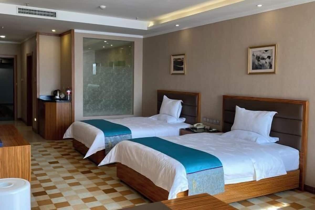 A hotel room with two beds, a desk, a chair, a phone, and a window.