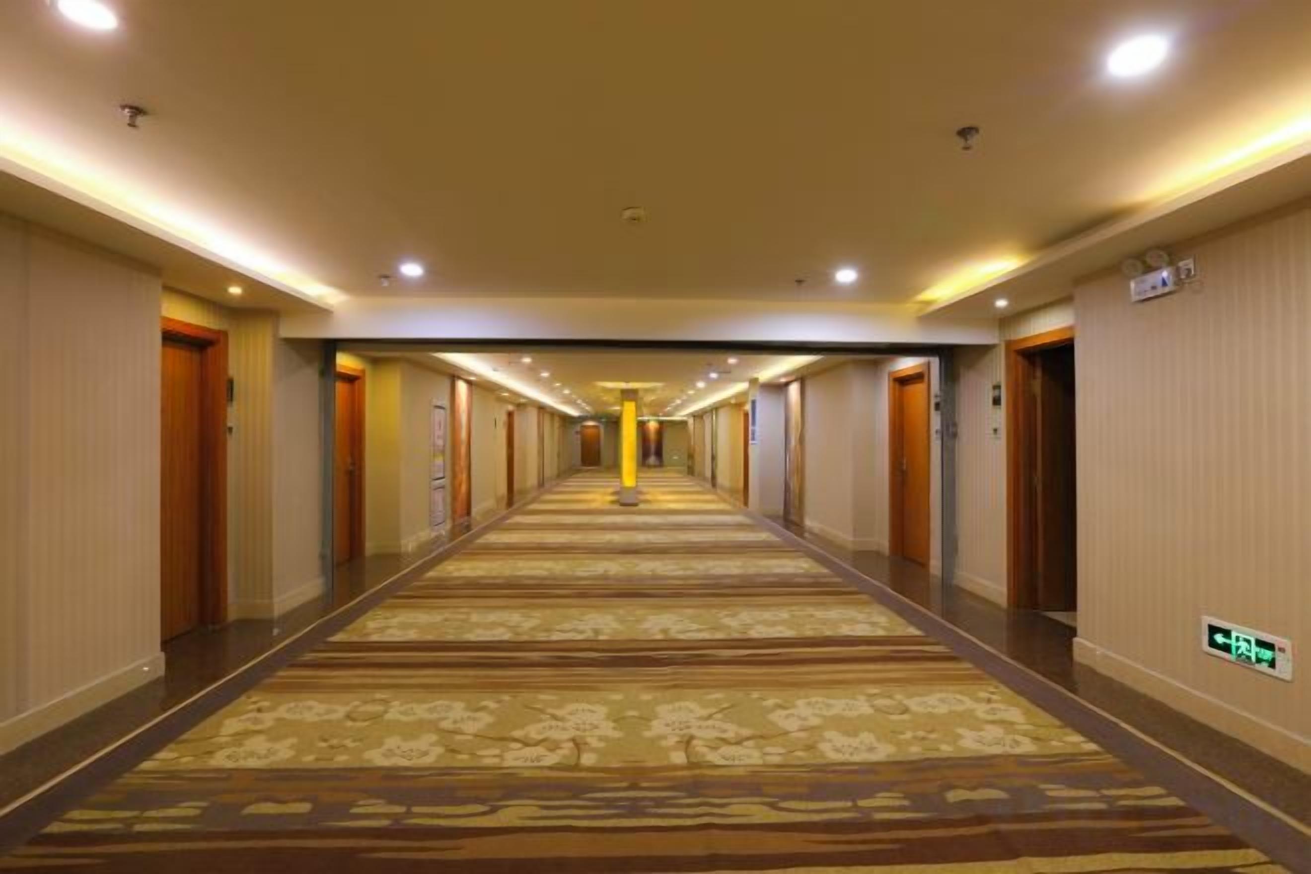 A hotel corridor with carpeted floors, doors on both sides, and overhead lighting.