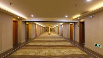 A hotel corridor with carpeted floors, doors on both sides, and overhead lighting.