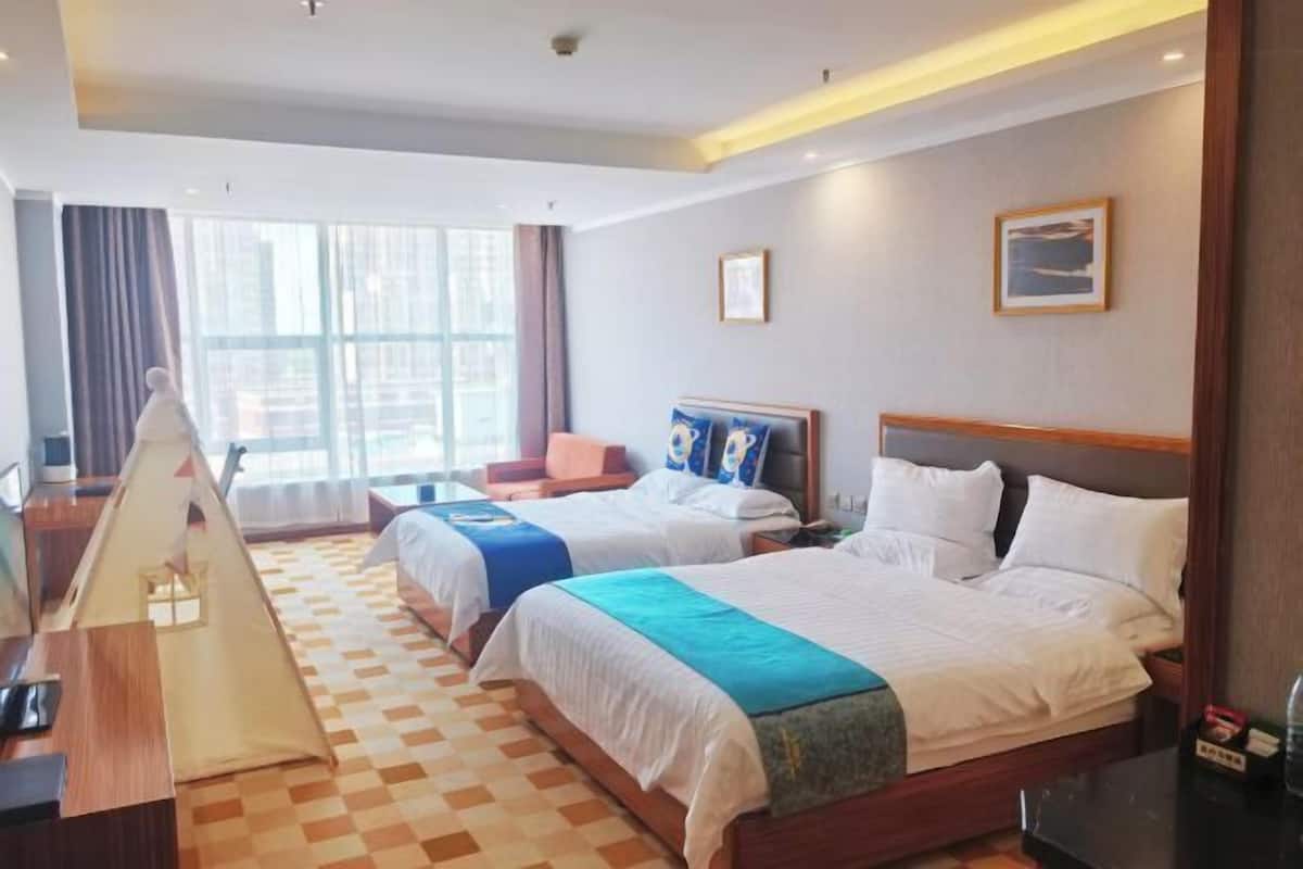 A hotel room with two beds, a desk, a chair, a tent, and large windows.