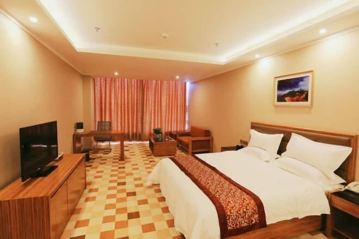 A hotel room with a checkered floor, a bed with white linens, a television, a desk, and a chair.