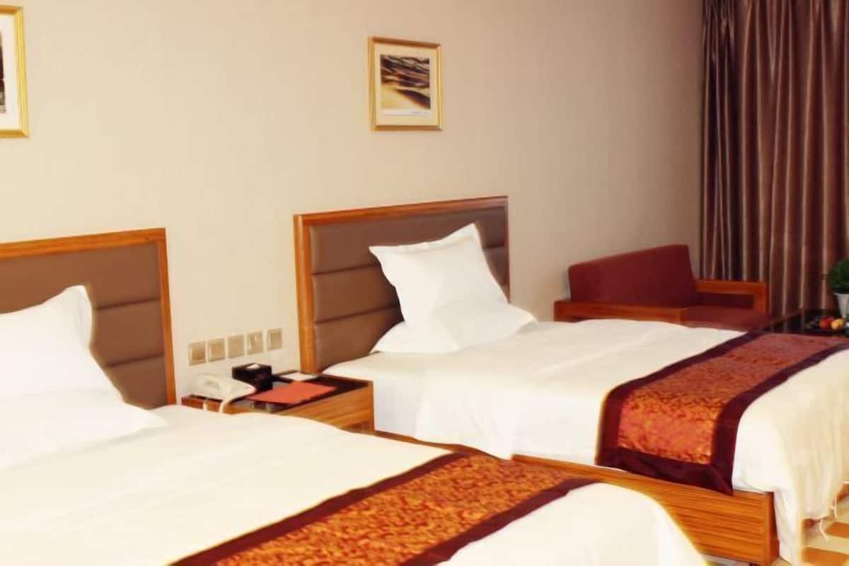 A hotel room with two beds, a wooden headboard, a red chair, a telephone, and a framed picture on the wall.