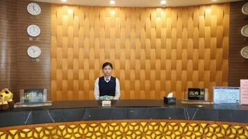 A reception desk with a patterned wall, clocks, and a person seated behind it.