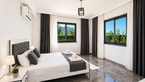 Habitación de hotel moderna con una cama grande, una mesita de noche con lámpara, un aplique de techo y dos ventanas con vistas a zonas verdes.