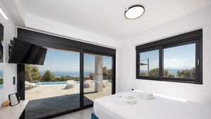 Un dormitorio moderno con cama, televisión y vistas a una piscina exterior y paisaje.