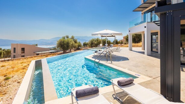 A modern pool area with a view of the sea, lounge chairs, and umbrellas.