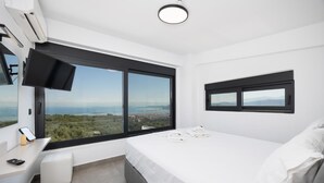 A modern bedroom with a large window, a flat-screen TV, and a bedside table with a phone and remote.
