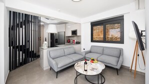 Un espacio habitable moderno con un sofá gris, una mesa de centro de mármol y una zona de cocina al fondo.