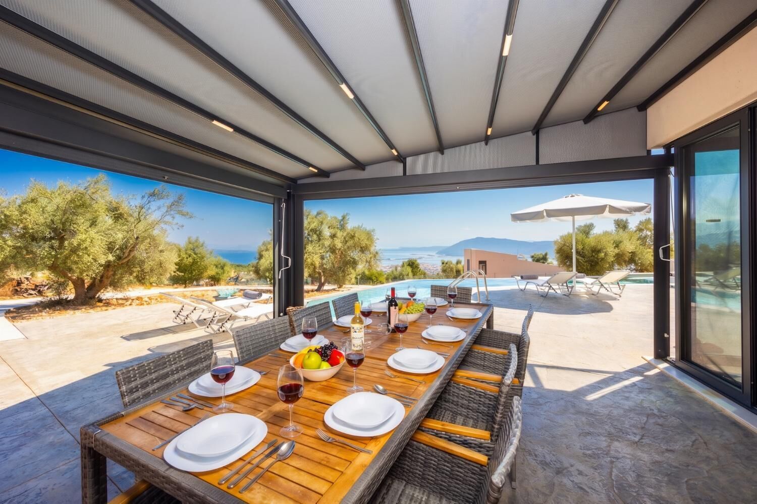Un'area pranzo all'aperto con vista sul mare e sulle montagne, una piscina e posti a sedere all'esterno.
