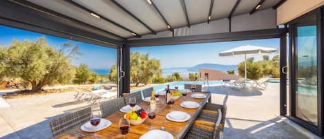 An outdoor dining area with a view of the sea and mountains, a pool, and outdoor seating.