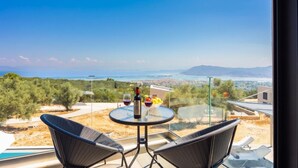 A balcony with a glass table, two chairs, a bottle of wine, and a bowl of fruit.
