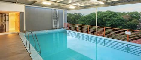 An indoor swimming pool with a view of trees, a ladder, and a railing.