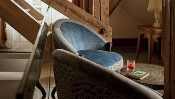 Una habitación acogedora con una escalera de madera, un sillón azul, un sofá estampado y una mesita con un libro y un vaso.