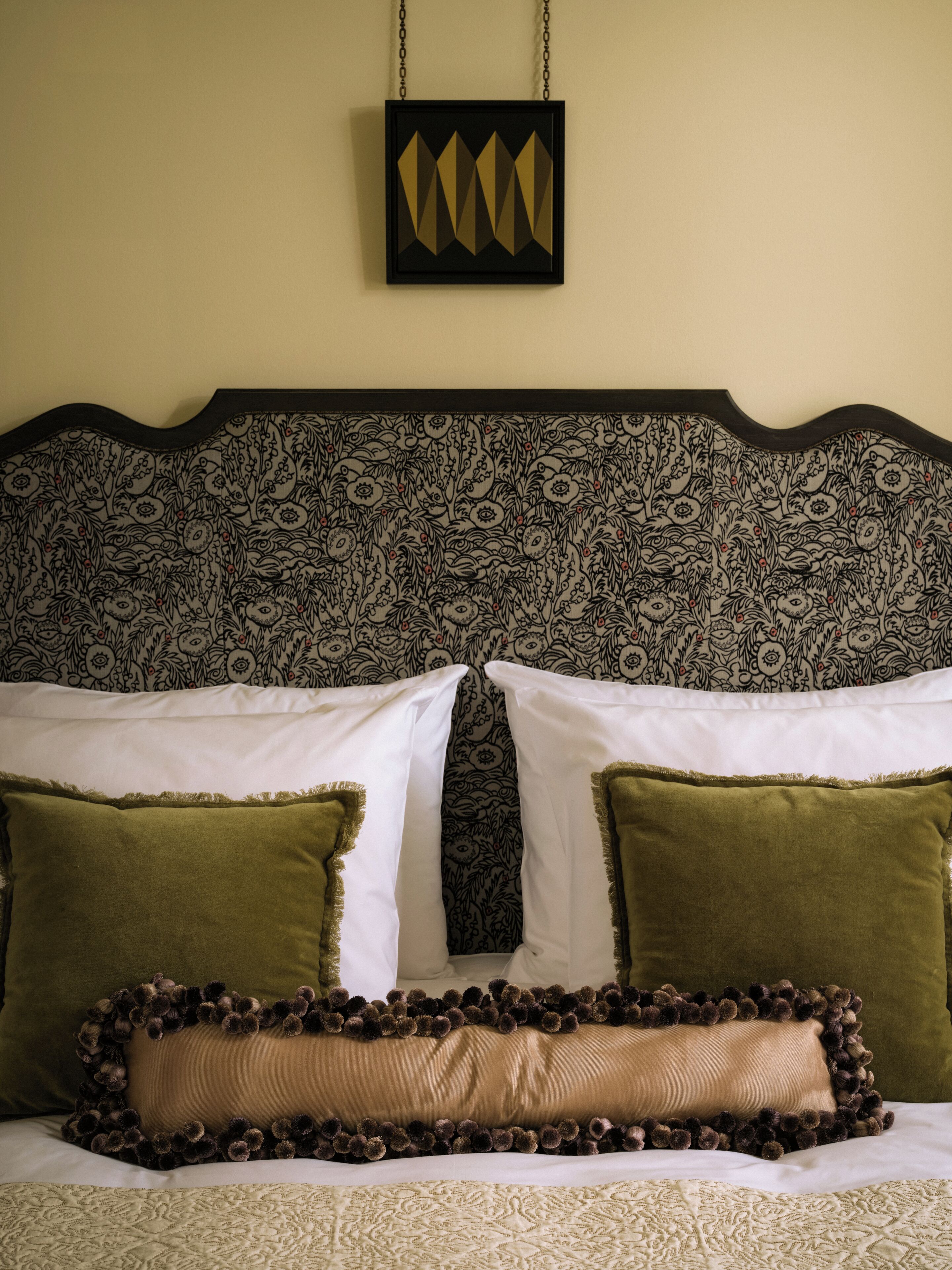 Una cama con un cabecero estampado, dos almohadas y un cojín decorativo con flecos.