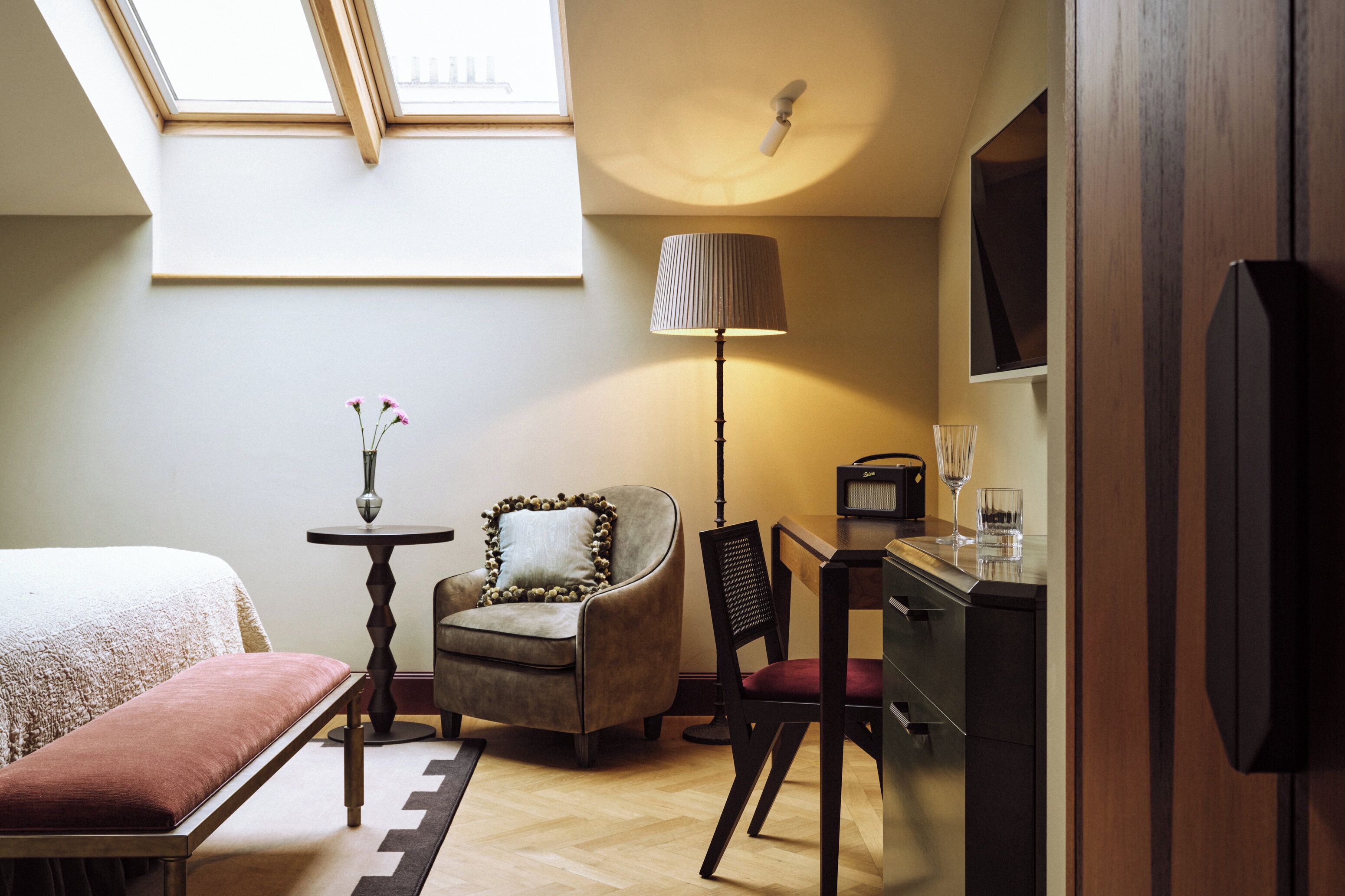 A bedroom with a bed, a chair, a desk, a lamp, and a TV.