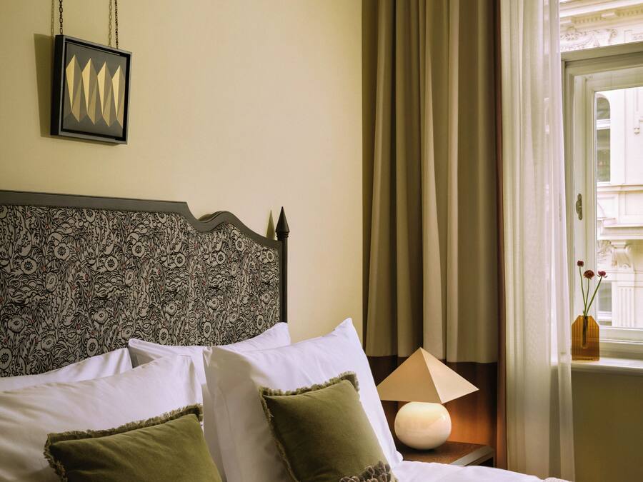 A neatly made bed with white and green pillows, a patterned headboard, and a bedside lamp.